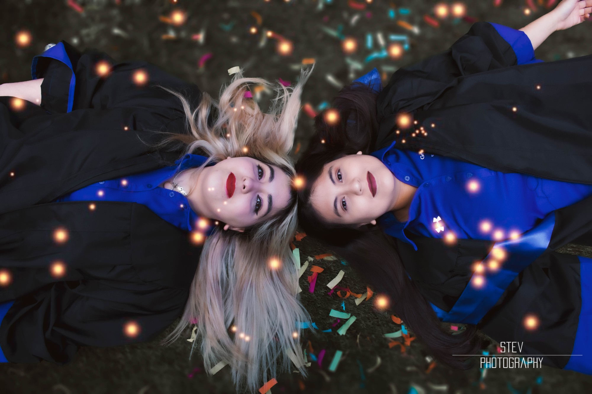 Graduation portrait of two graduates lying in confetti, by @stevfilmstudios