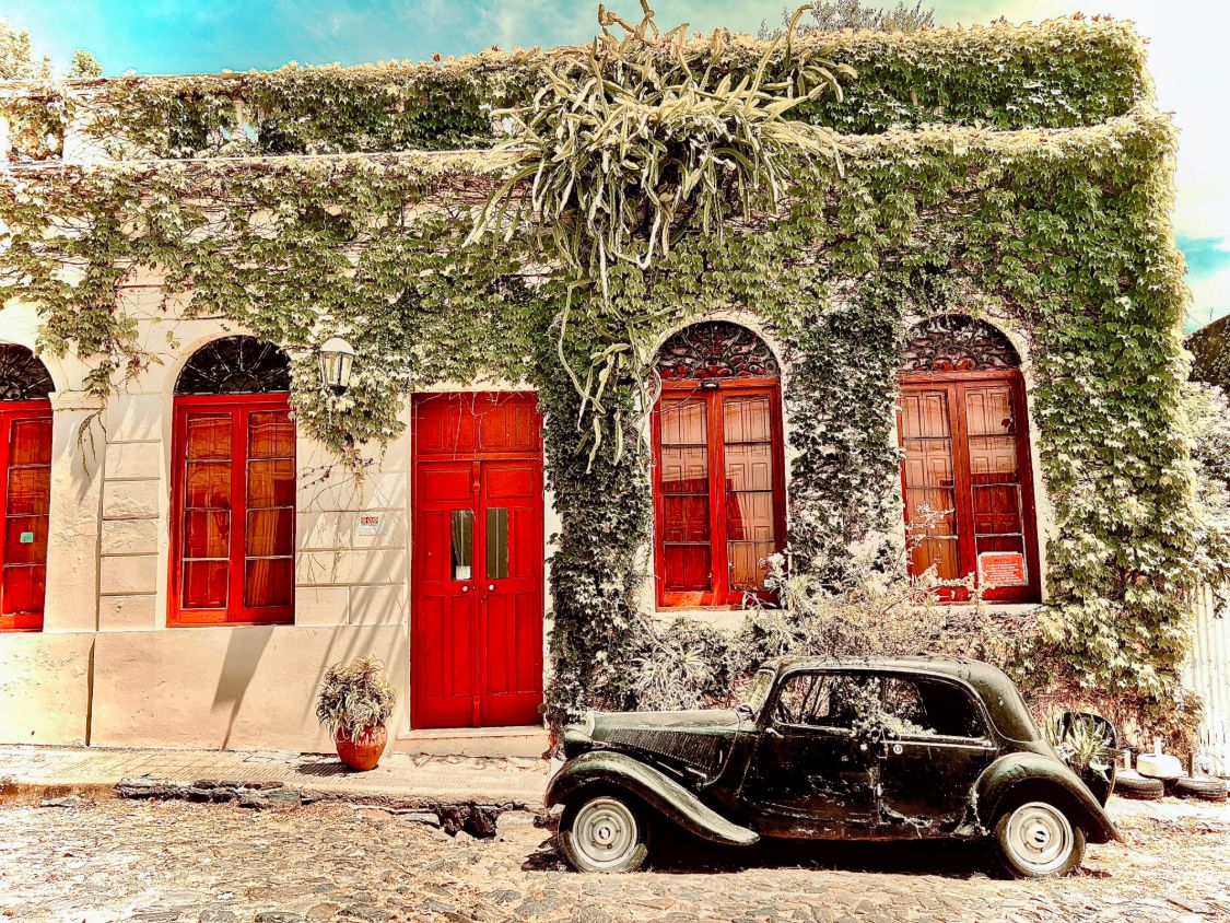 Vintage black car parked on a cobblestone street in front of an ivy-covered building with red doors, by @stevfilmstudios